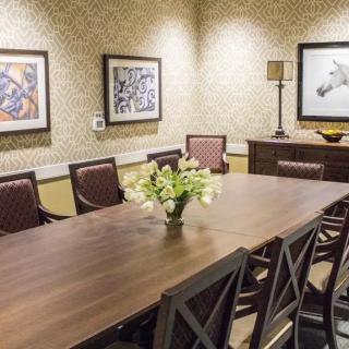 A well-decorated conference room featuring a large meeting table surrounded by chairs, with artwork on the walls and a decorative lamp.