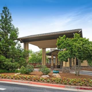 A modern building entrance surrounded by trees and landscaped gardens.