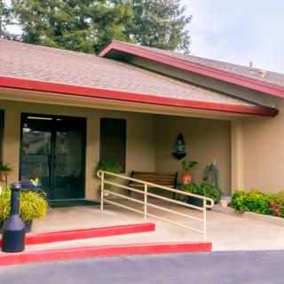 A building entrance with a ramp and bench, surrounded by plants.