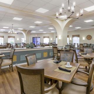 A spacious dining area with neatly arranged tables and chairs, illuminated by elegant chandeliers.