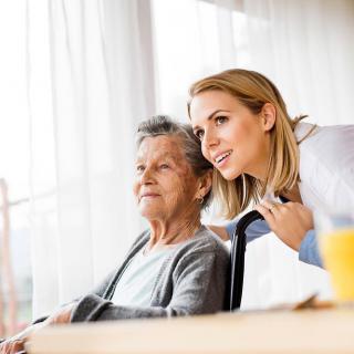 A younger woman providing care and companionship to an elderly woman in a home setting.