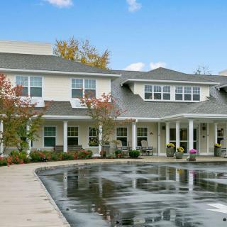 A two-story residential building with a pond and trees in the foreground.
