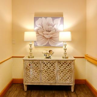 A stylish hallway featuring a decorative console table with two lamps and a large flower painting above.