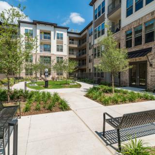 A modern apartment complex with a landscaped courtyard featuring benches and trees.