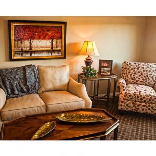 A cozy living room with a sofa and armchair, adorned with a lamp and painting for decor.