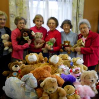A group of seniors holding teddy bears, surrounded by a collection of stuffed animals indoors.