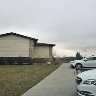 A cloudy day featuring a residential building with parked cars along the sidewalk.