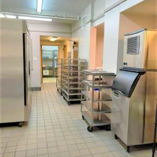 A well-organized commercial kitchen featuring stainless steel refrigeration units and food storage carts.