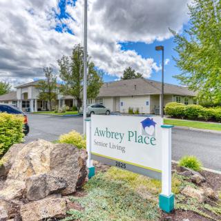 A sign for Aubrey Place Senior Living in front of a residential building on a cloudy day.