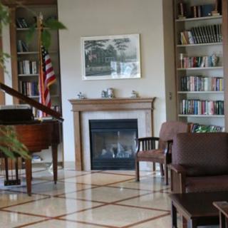 A cozy lounge area featuring a fireplace, piano, bookshelves, and seating.