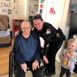 A police officer shares a joyful moment with an elderly person in a wheelchair, while a young child looks on.