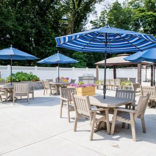 An outdoor patio area with tables, chairs, and blue umbrellas on a sunny day.