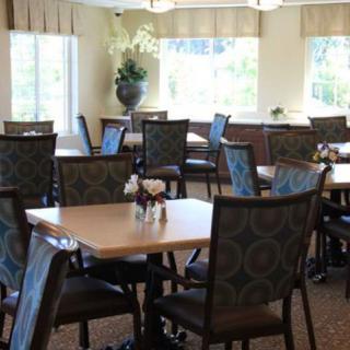 An empty dining room with neatly arranged tables and chairs, illuminated by natural light from large windows.