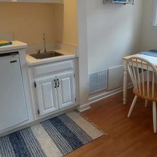 A compact kitchenette with a sink, mini fridge, and adjacent dining area featuring a small table and chairs.