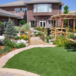 A beautifully landscaped garden with a lush lawn, pathway, and wooden bridge in front of a modern house.