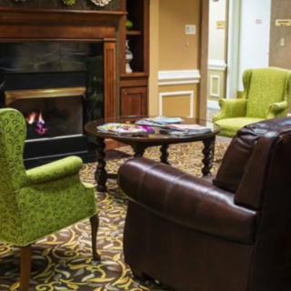 Cozy living room with a fireplace, green chairs, and a leather sofa.