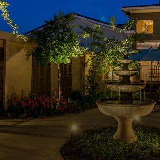 A serene nighttime courtyard featuring a lit fountain surrounded by trees and a building.