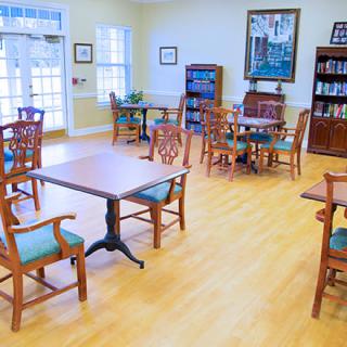 A bright community room with tables, chairs, and bookshelves.
