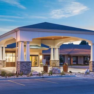 A building with a covered entrance featuring columns and a landscaped area, set against an evening sky.