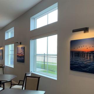 A modern interior space featuring large windows and wall art, with tables and chairs arranged nearby.