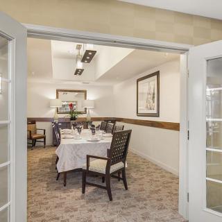 A well-decorated dining room with a set table and elegant chairs, viewed through open French doors.
