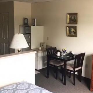 A cozy apartment with a small dining area featuring a table and chairs, adjacent to a lamp and decorated with framed paintings.
