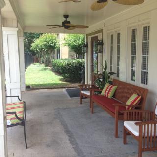 A cozy porch with comfortable seating, a rug, and ceiling fans, overlooking a garden.