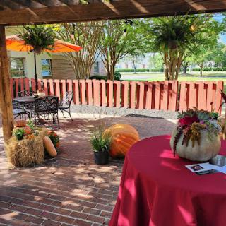 A cozy outdoor patio area decorated for a fall event, featuring pumpkins and vibrant plants.