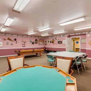 A spacious game room featuring a pool table and card tables, with pink walls adorned with various decorations.