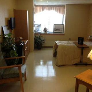 A tidy and well-lit hospital room with a bed, chair, and plants near the window.