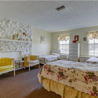 A cozy bedroom with twin beds and floral bedding, featuring bright windows and decorative wall elements.
