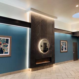 A modern lobby with blue walls, featuring abstract artwork and a central illuminated mirror.