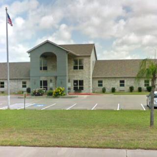 A building with a flagpole, surrounded by a parking lot and well-maintained lawn.