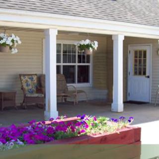 A cozy porch with flowers, hanging plants, and outdoor seating.