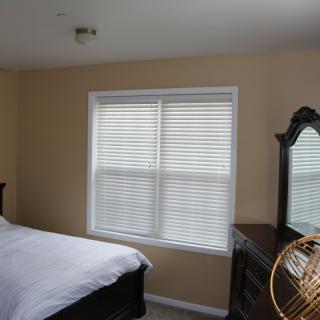 A cozy bedroom with a bed, dresser, and window with blinds.