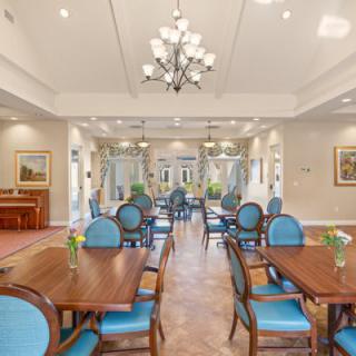 An elegant dining room featuring blue upholstered chairs, wooden tables, and a central chandelier.