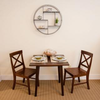 A cozy dining area with a wooden table set for two, accompanied by matching chairs and complemented by a circular wall shelf.