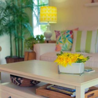 A cozy living room with a coffee table adorned with yellow flowers, surrounded by a sofa with colorful cushions and soft lighting.