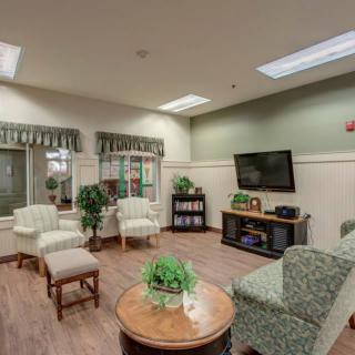 A cozy living room with comfortable seating, a television, bookshelves, and indoor plants.