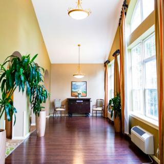 A bright and spacious lobby with large windows, wooden flooring, and potted plants.