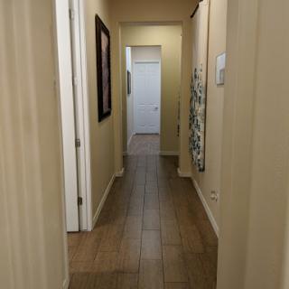 A well-lit hallway leading to a closed door, featuring neutral walls and tiled flooring.