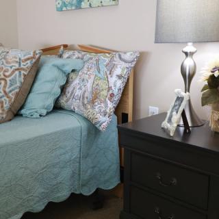 A cozy bedroom corner with a neatly made bed, decorative pillows, and a stylish nightstand lamp.