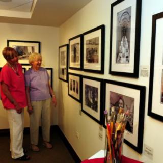 Two visitors admire framed artworks in a gallery setting.