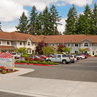 A residential building with a parking lot and several cars parked in front, surrounded by trees.