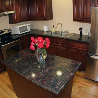 A modern kitchen with granite countertops and wooden cabinets, featuring a centralized island adorned with flowers.