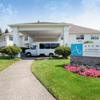 The entrance to a building with a covered driveway and a parked van, surrounded by well-maintained landscaping and signage.