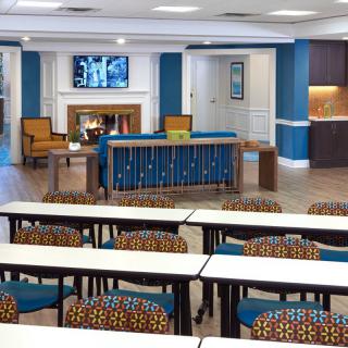 A modern classroom with tables, colorful chairs, and a television near the fireplace.