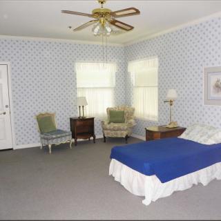 A spacious bedroom with blue decor, featuring a single bed, armchairs, and a ceiling fan.