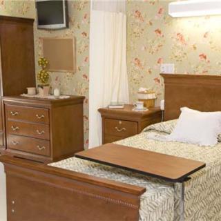 A hospital room with a bed, overbed table, and wooden furniture.