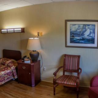A cozy bedroom with a bed, nightstand, lamp, chair, and wall painting.